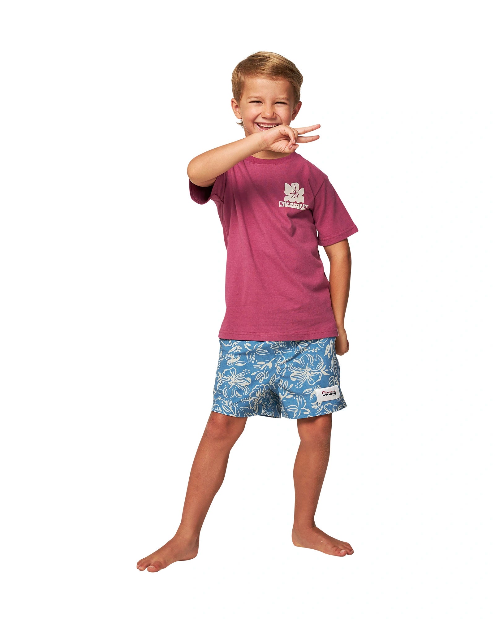 Full body front view of a little boy posing a peace hand sign wearing the Okanui Kids swim shorts in Steel