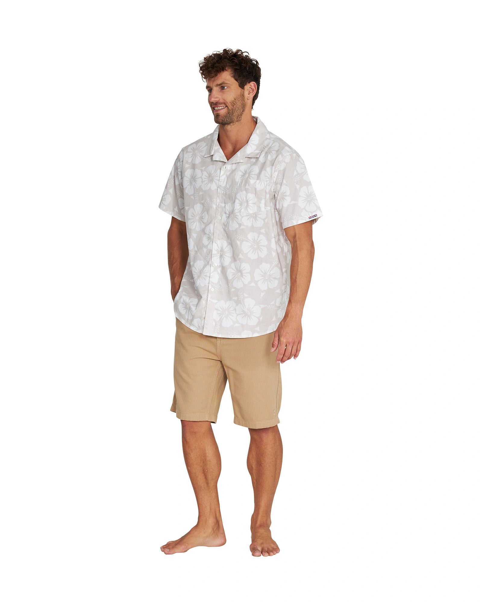 Full body angled left side view of a male model wearing the Okanui Classic Button up short sleeve shirt in Hibiscus Stone