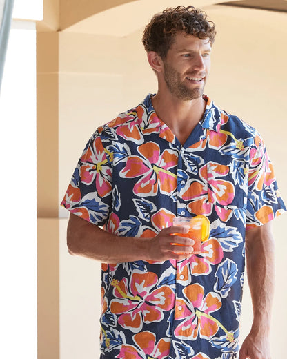 A male model holding a cocktail wearing the Okanui Rhapsody Aloha Short Sleeve Shirt in navy multi.