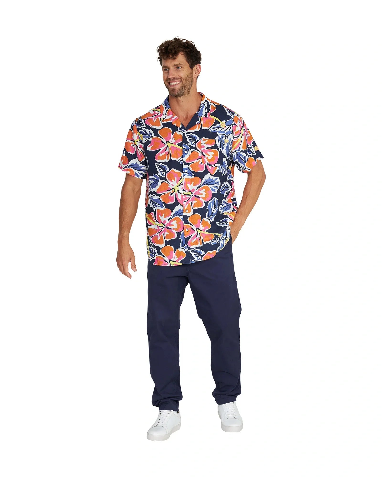 Full body view of a male model wearing the Okanui Rhapsody Aloha Short Sleeve Shirt in navy multi, navy pants and white shoes.