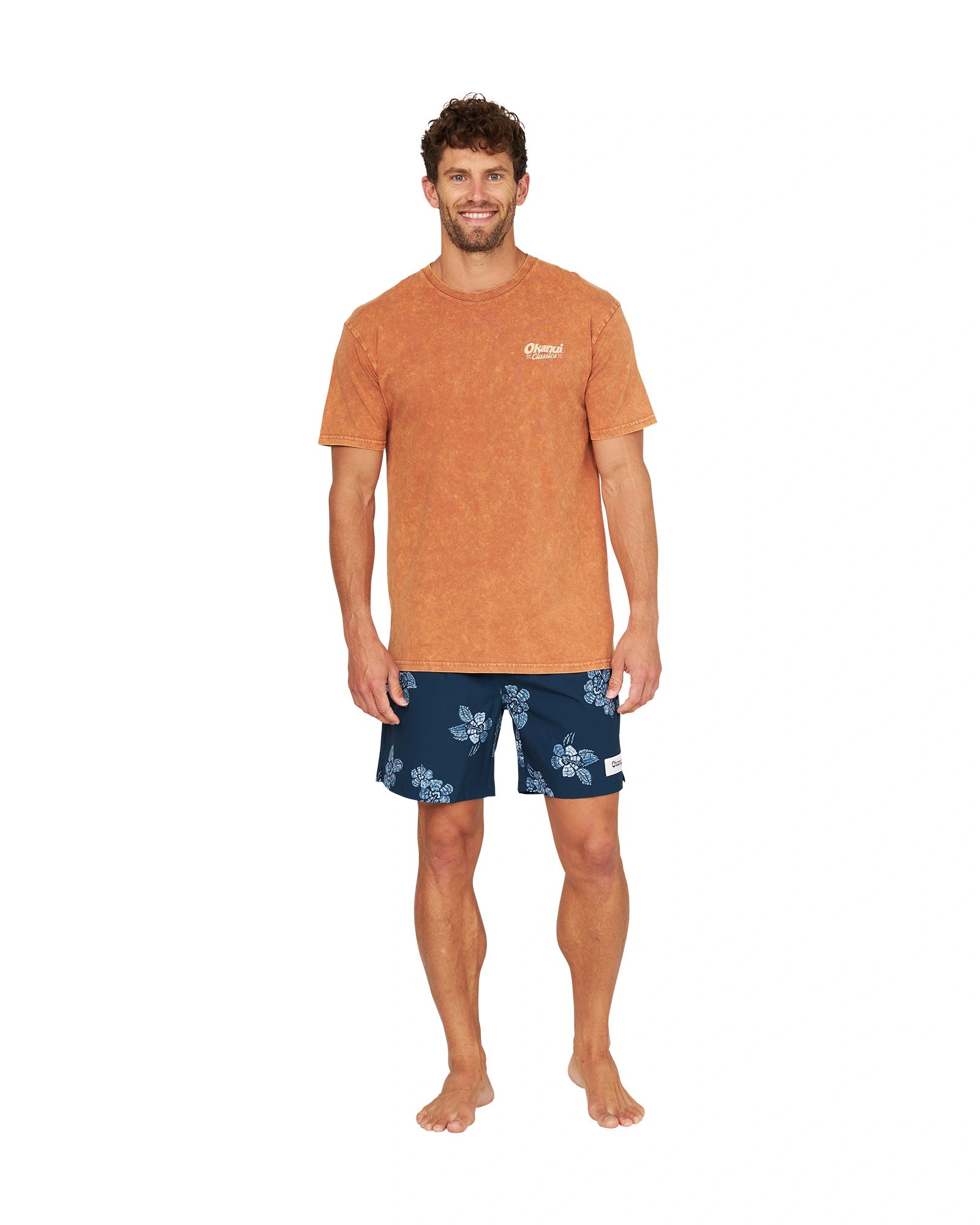 A male model posing casually wearing the Okanui Big Screen T-Shirt in rust color.