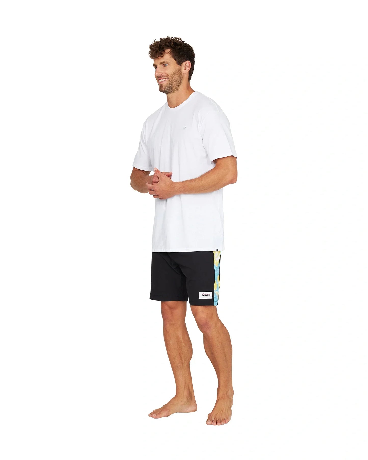 A male model wearing the Okanui Sidelines Boardrider Boardshort in Black and a white t-shirt.