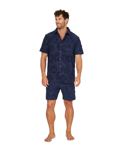 A full body view of a male model wearing the Okanui Terry Jacquard Shirt in Hibiscus Navy and terno shorts.