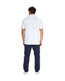 Full body back view of a male model wearing the Okanui Starboard Short Sleeve Shirt in Hibiscus white wearing navy pants and white shoes.