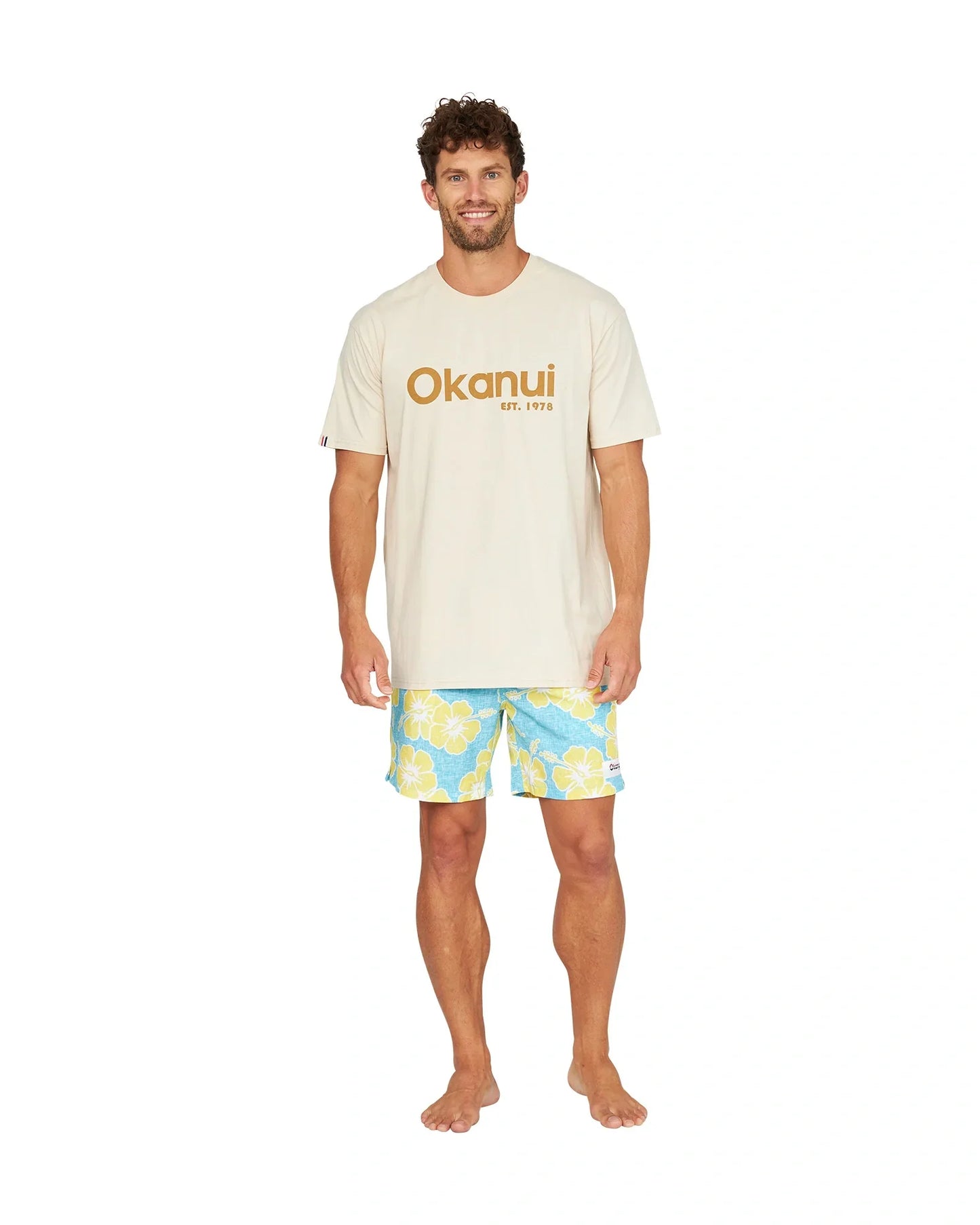 A male model wearing the Okanui Way Back When Stretch Swim Short in Aqua Yellow and a birch Okanui Logo Tee.