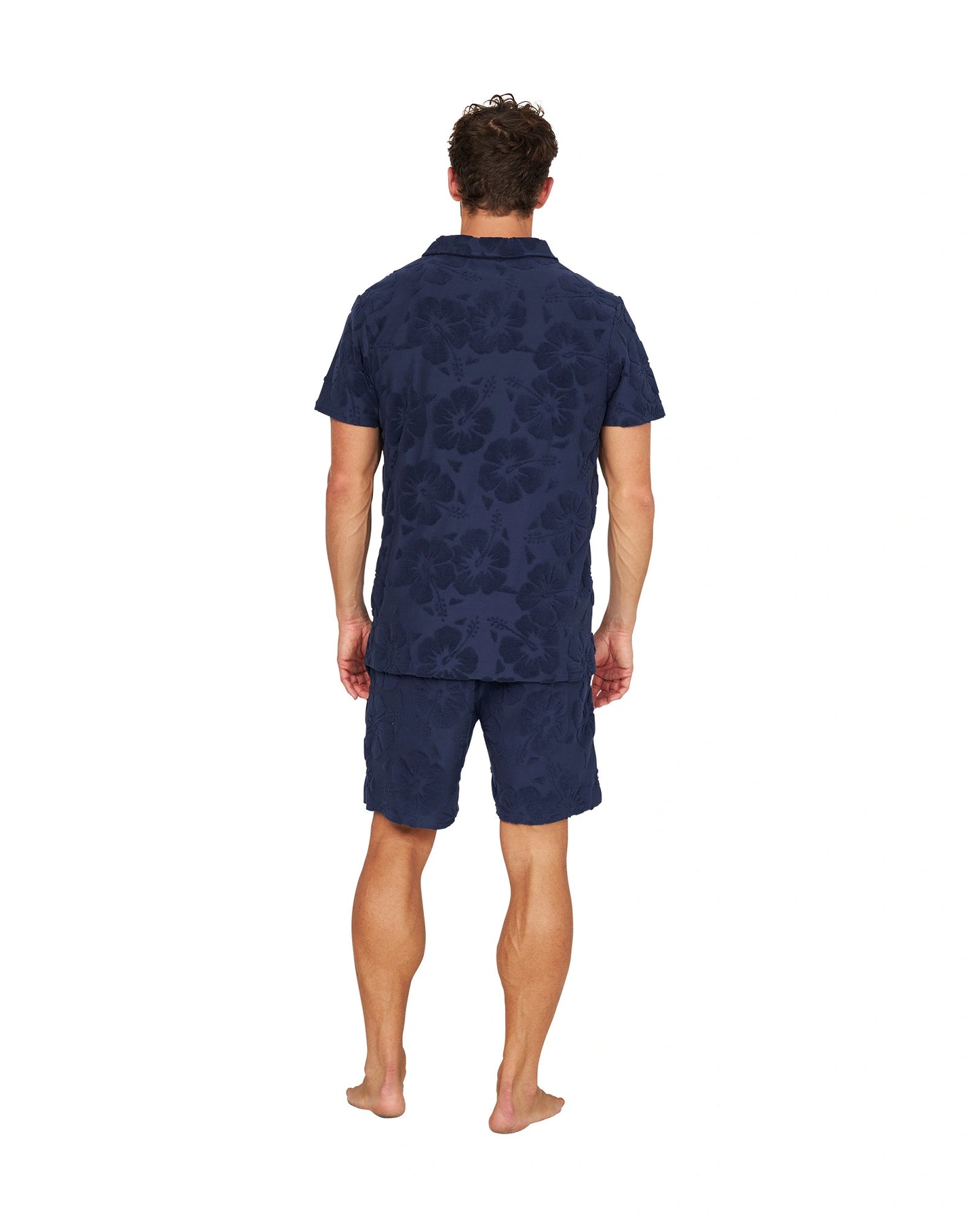 Full body back view of male model wearing the Okanui Weekend Terry Jacquard Polo in Hibiscus Navy with terno shorts.