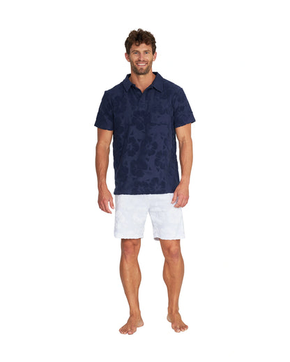 Full body front view of male model wearing the Okanui Weekend Terry Jacquard Polo in Hibiscus Navy with white shorts.