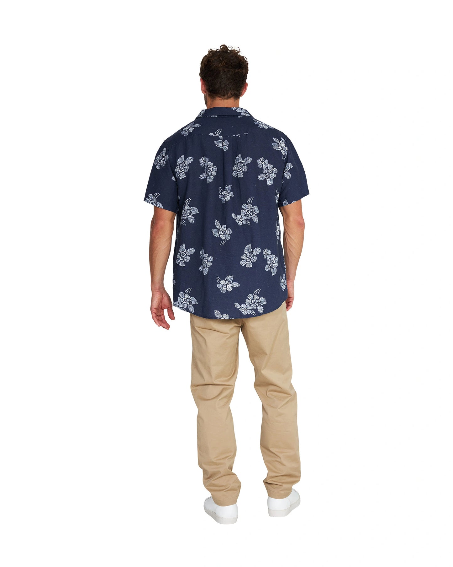 Back view of a male model wearing the Okanui Whitewater Aloha Short Sleeve Shirt in navy color with khaki pants and white shoes.