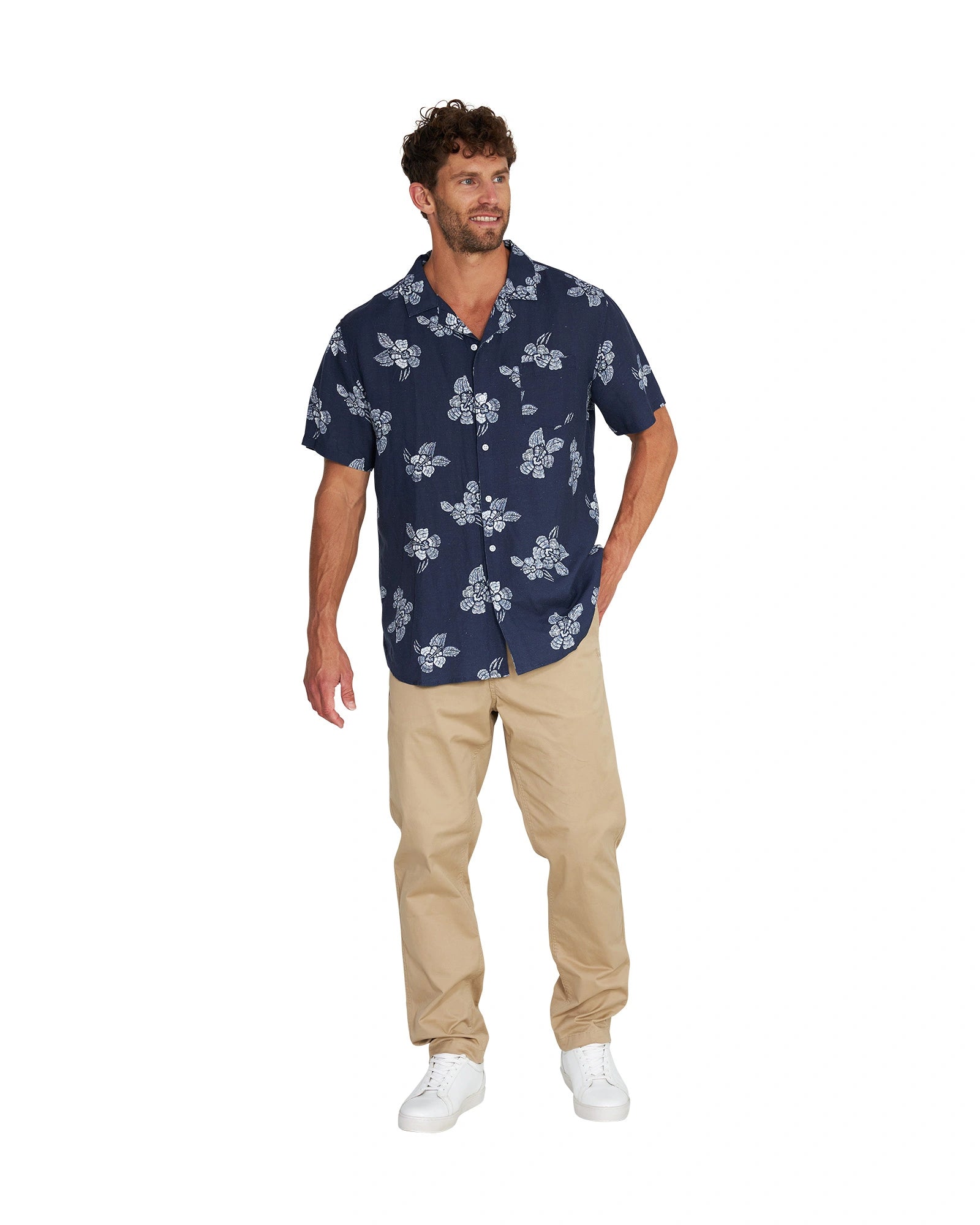 A male model wearing the Okanui Whitewater Aloha Short Sleeve Shirt in navy color with khaki pants and white shoes.