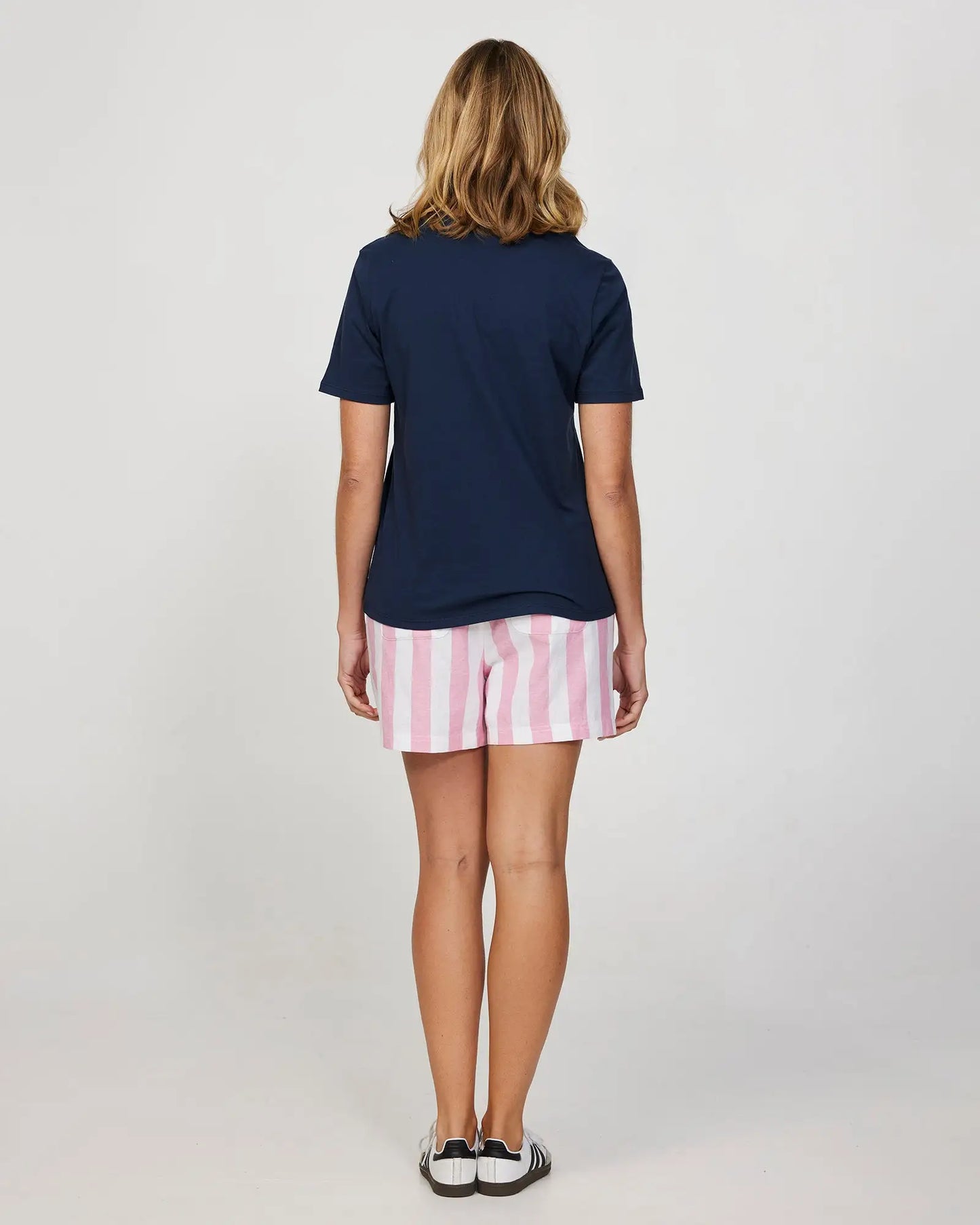 Full body back view of a female model wearing the Okanui Womens Holiday Beach Short in Classic Stripe Pink