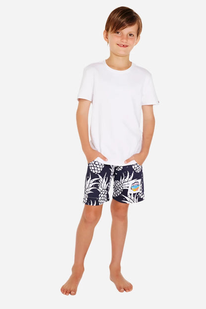 A pair of Okanui kids classic shorts with a white and navy color pineapple patterned.