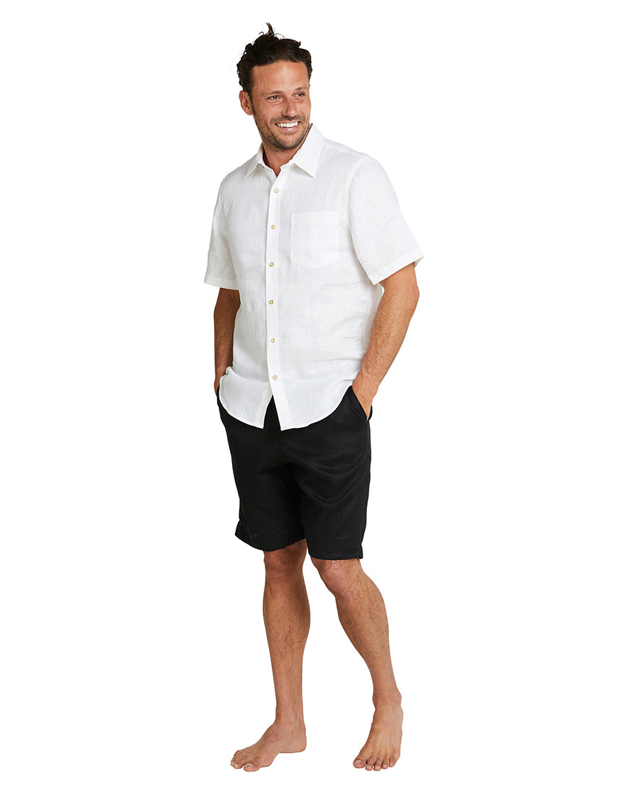 A smiling model wearing black shorts and the Okanui Linen Short Sleeve Shirt in white color.