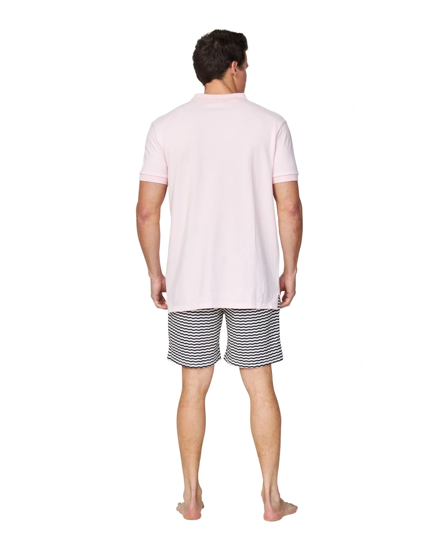 A full body length back view of a male model wearing a black and white striped short and the Okanui Classic Polo Shirt in pale pink colour.
