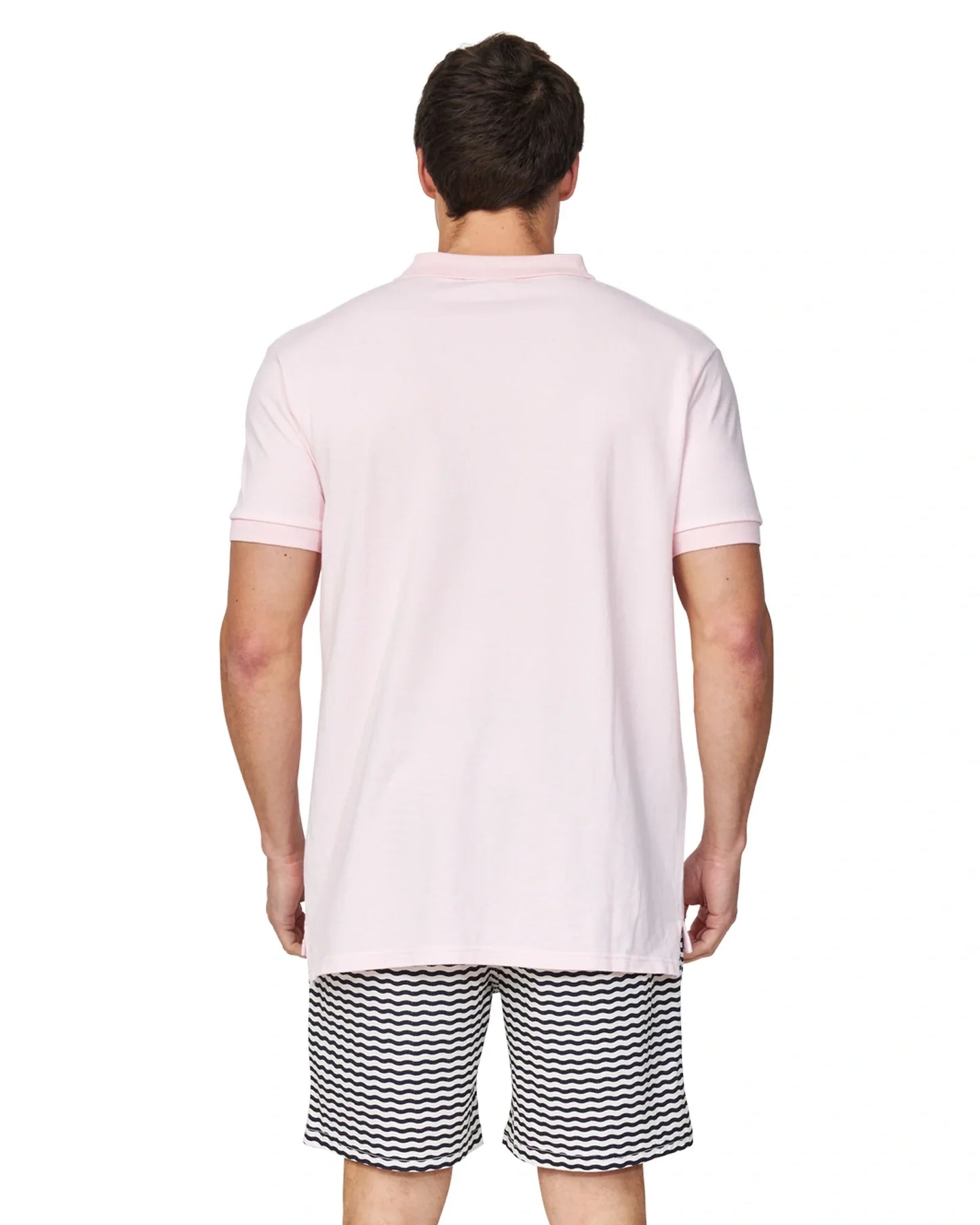 A closer back view of a male model wearing a black and white striped short and the Okanui Classic Polo Shirt in pale pink colour.