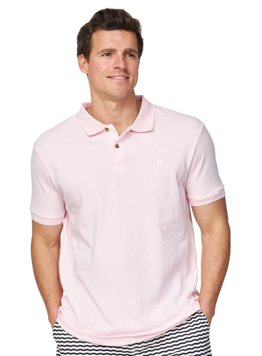 The Okanui Classic Polo Shirt in pale pink color worn by a model casually posing with his hands in his pocket.