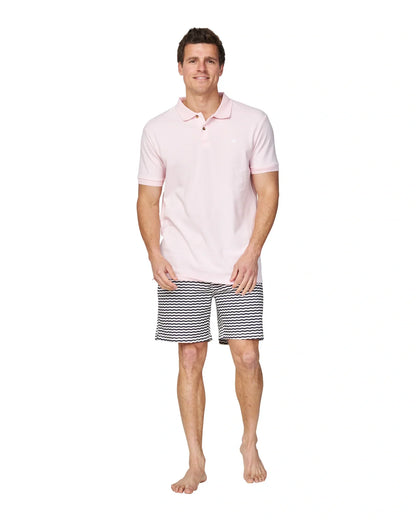A full body length view of a male model wearing a black and white striped short and the Okanui Classic Polo Shirt in pale pink colour.