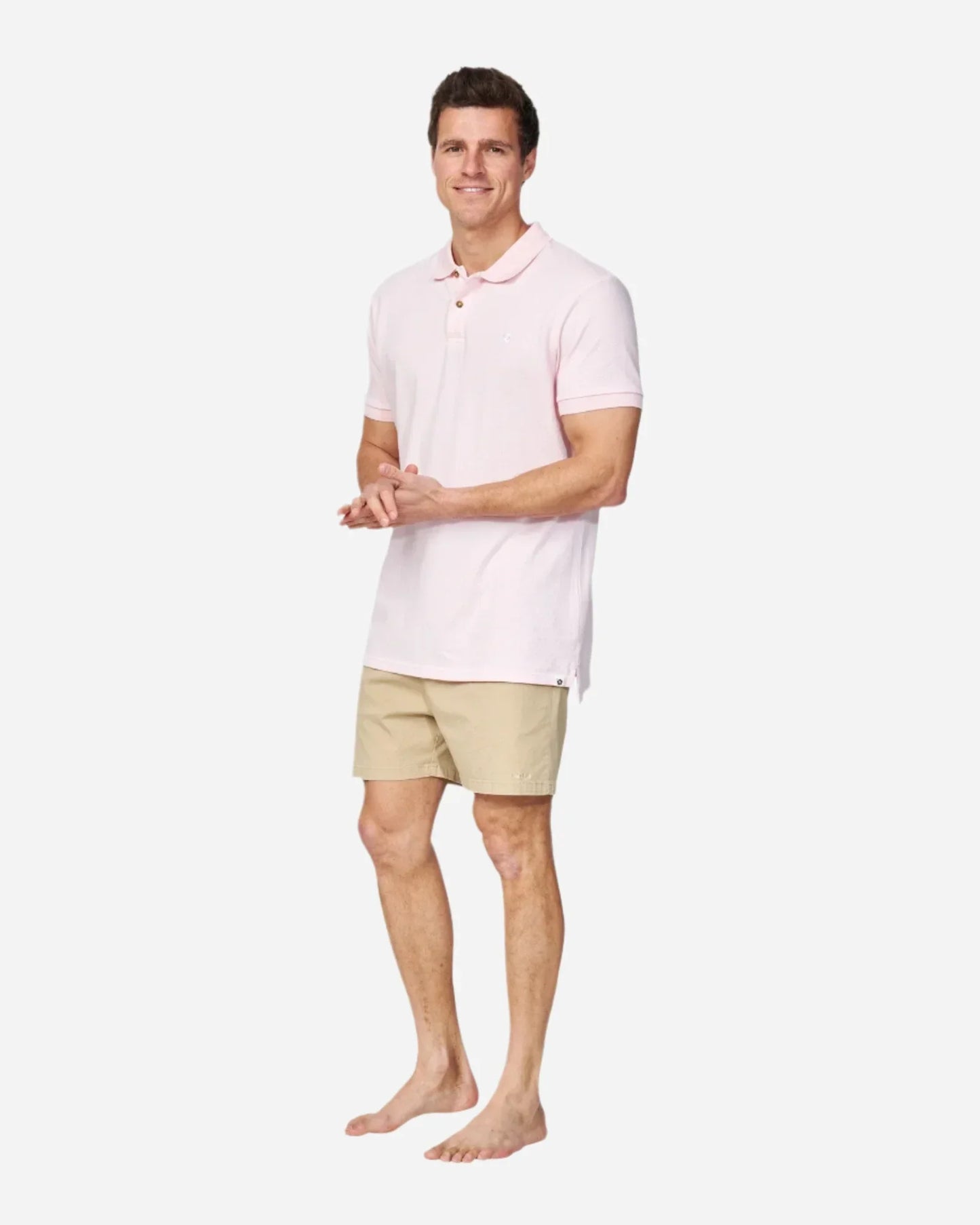A barefoot model wearing the Okanui Classic Polo Shirt in pale pink color paired with a walkshort.