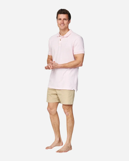 A barefoot model wearing the Okanui Classic Polo Shirt in pale pink color paired with a walkshort.