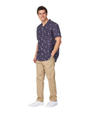 A male model posing with his hand on the pocket of his khaki pants and also wearing the Okanui Icons Coastal Short Sleeve Aloha Shirt in navy colour.