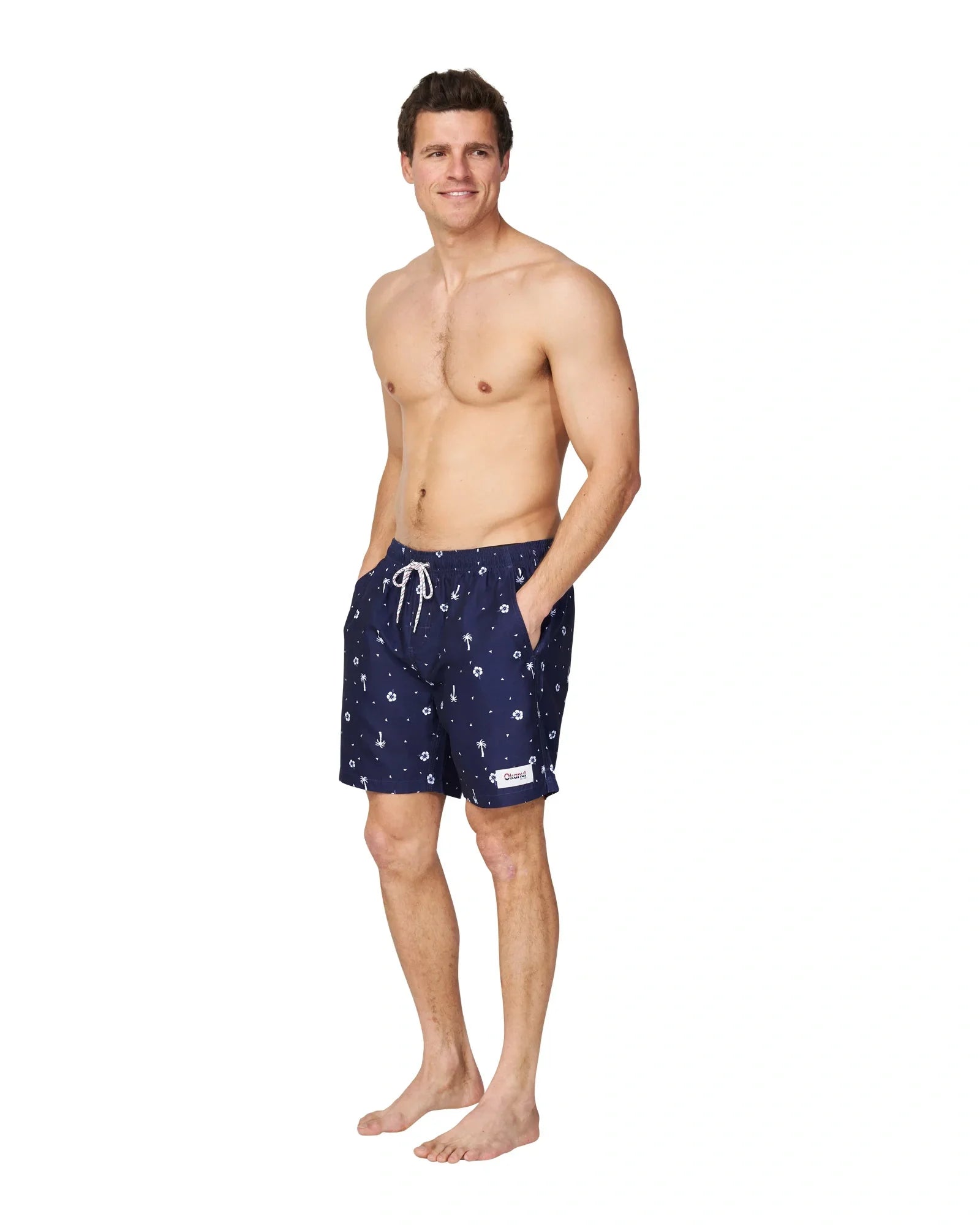 A male model wearing the Okanui Icons Swimshorts in navy colour with his hands in the pockets.
