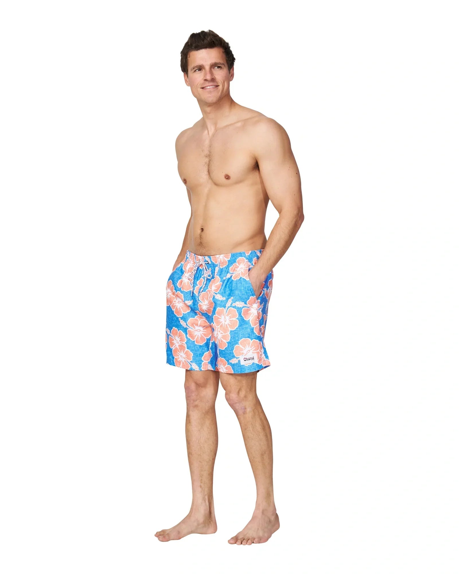 A male model wearing only the Okanui Way Back When Swimshorts in Bright Blue/Orange colour with his hands in the pockets.