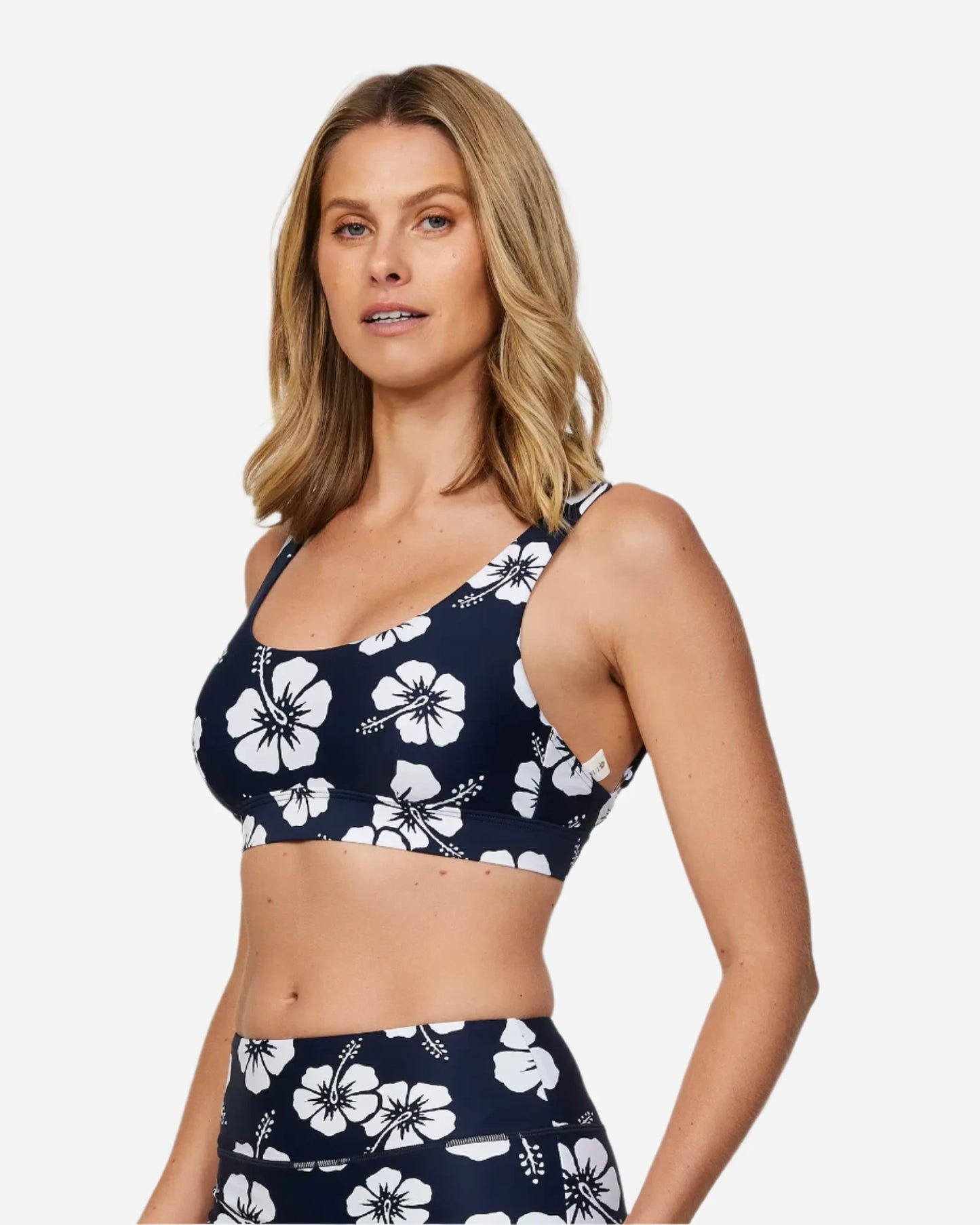 Front-left view of a female model wearing the Okanui Active Swim Crop Top in Hibiscus Navy