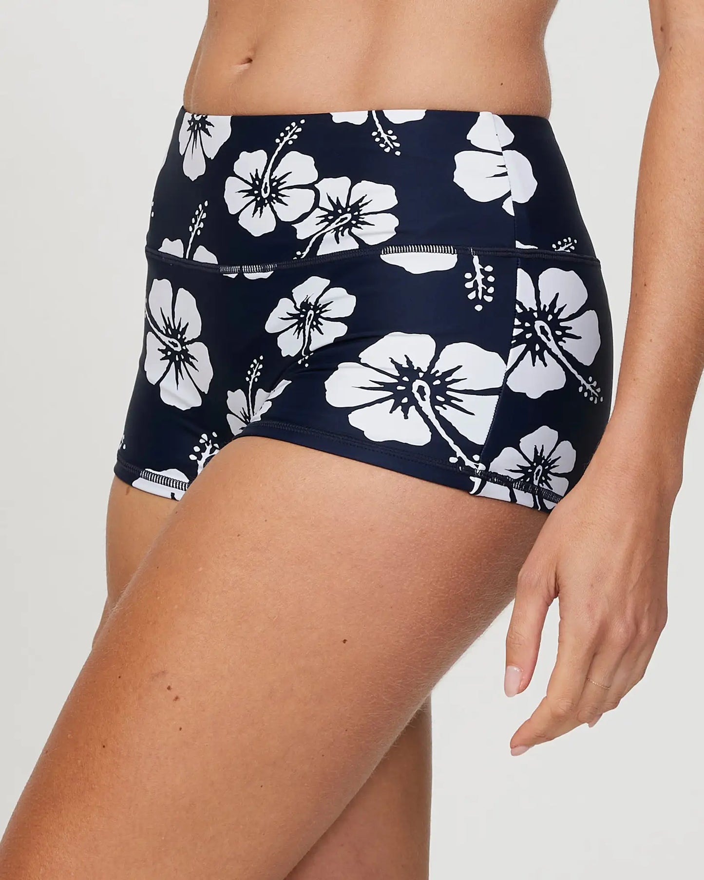 Closeup Left side view of a female model wearing the Okanui Active Swim Short in Hibiscus Navy