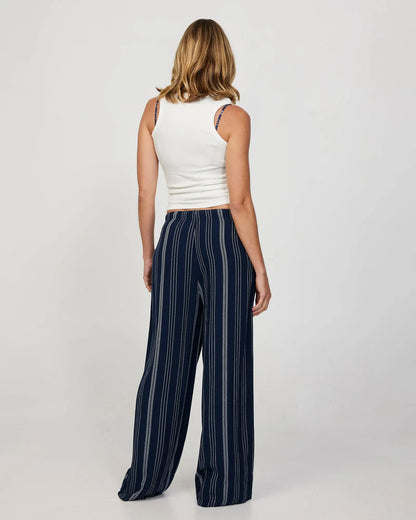 Back view of a female model wearing a loose white t-shirt and the Okanui women's beach pants in navy.