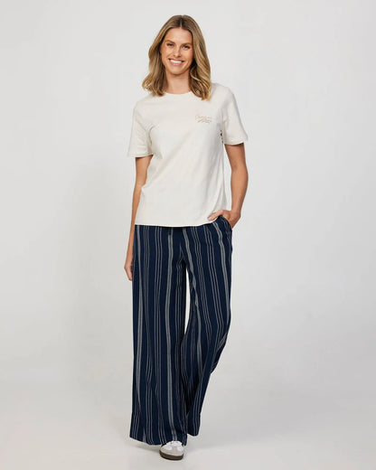 A female model wearing a loose white t-shirt and the Okanui women's beach pants in navy.