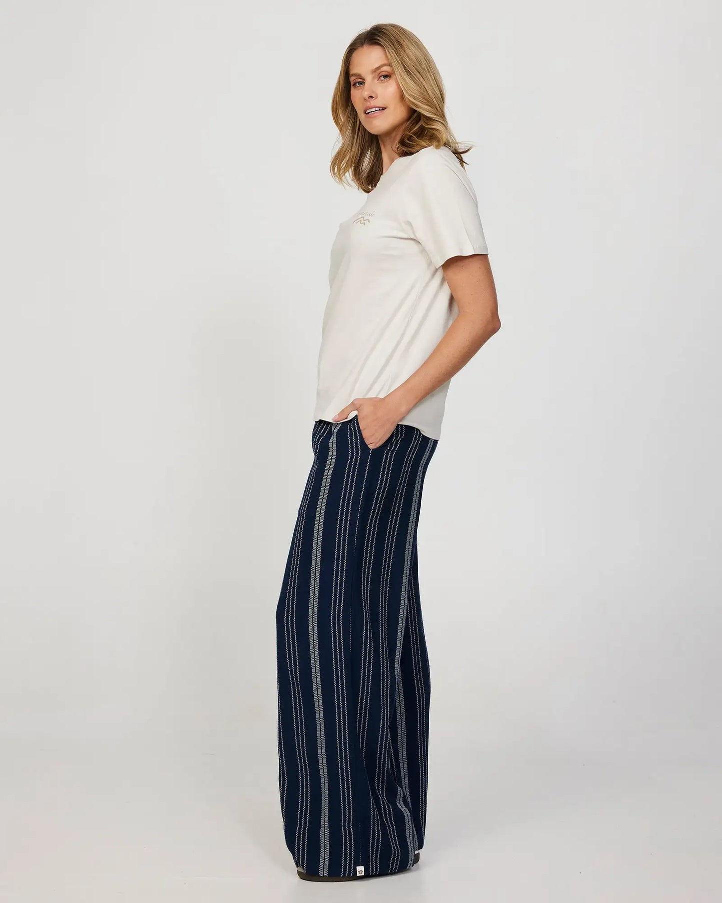 Side view of a female model wearing a loose white t-shirt and the Okanui women's beach pants in navy.