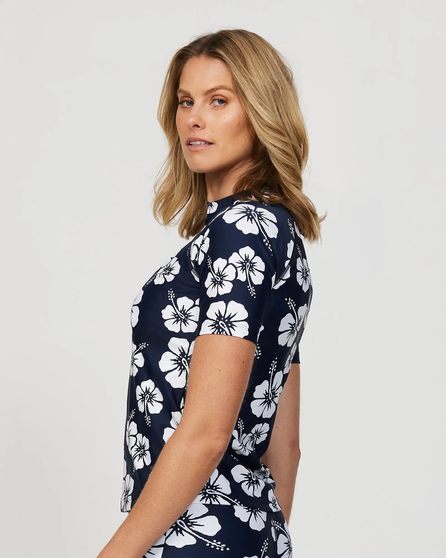 Left side view of a female model wearing the Okanui Short Sleeve Rash vest in Hibiscus Navy