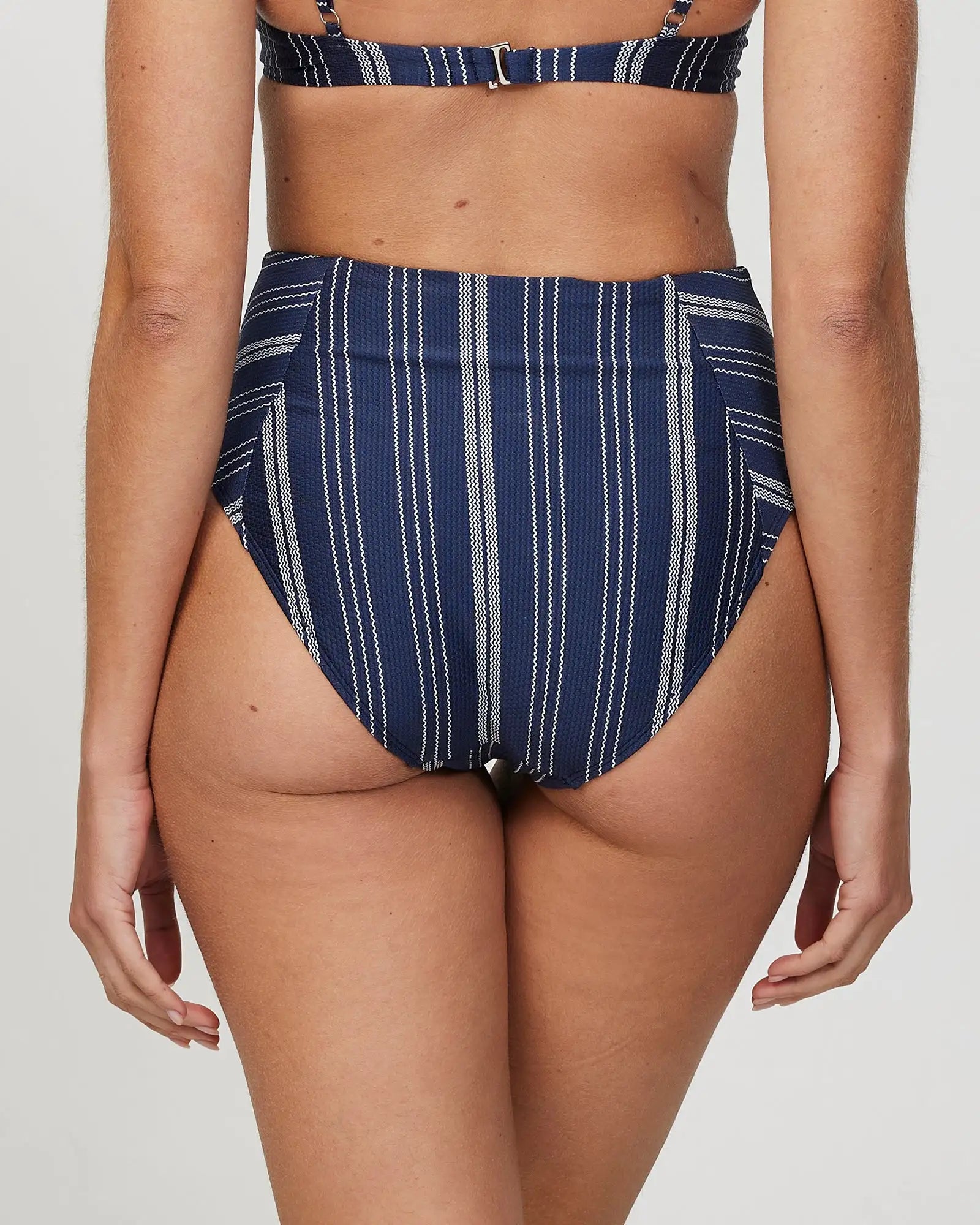 Back view of a female model wearing the Okanui Horizon High waist Bikini Bottom in Navy Stripe