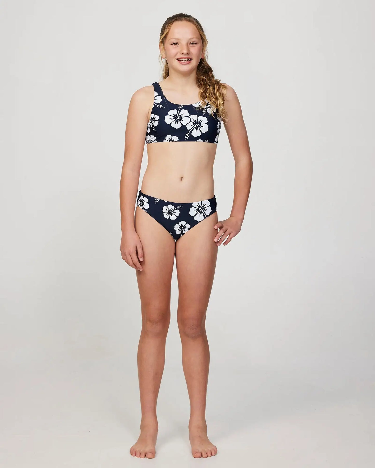 Full body front view of a girl model with her hand in her hips pose wearing the Okanui Crop Bikini Set in Hibiscus Navy