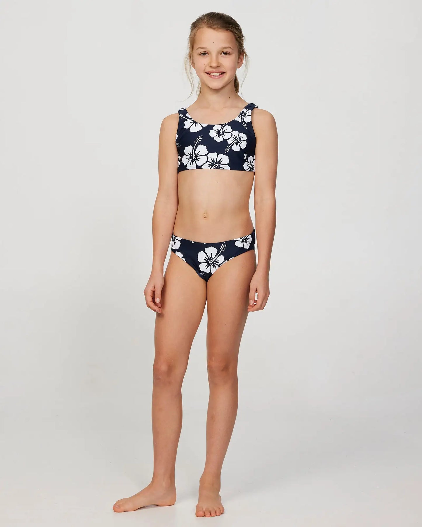 Full body front view of a little girl model wearing the Okanui Crop Bikini Set in Hibiscus Navy