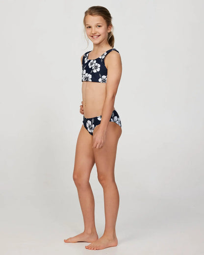 Full body left side view of a little girl model wearing the Okanui Crop Bikini Set in Hibiscus Navy