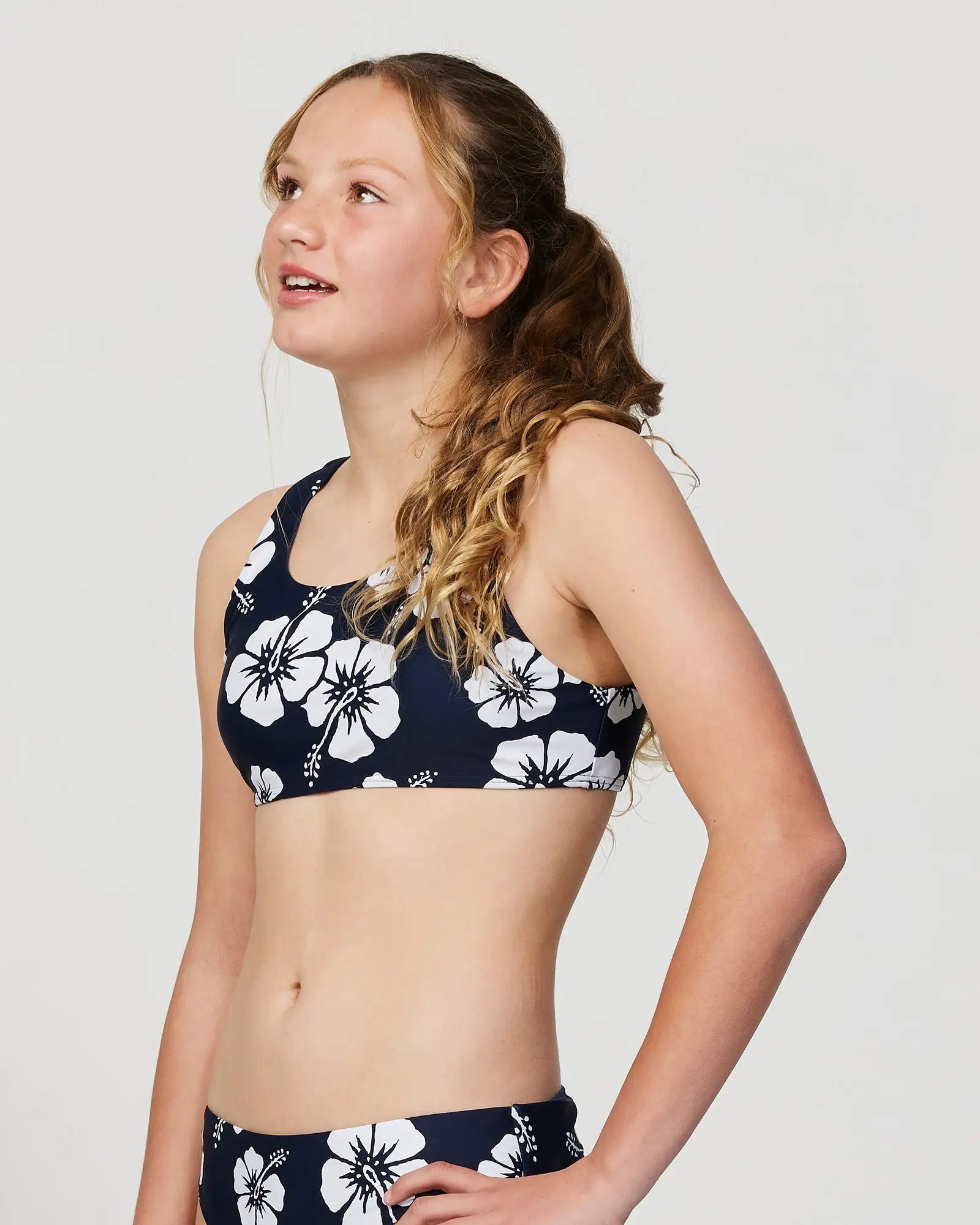 Closeup front-left view of a girl model wearing the Okanui Crop Bikini Set in Hibiscus Navy