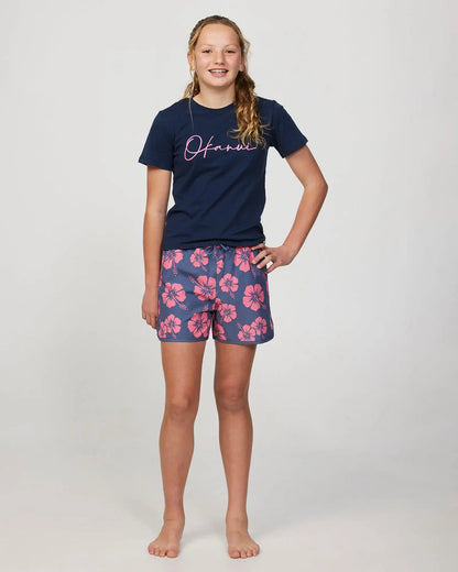 Full body front view of a girl model wearing the Okanui swim short for girls in Hibiscus Iron Pink