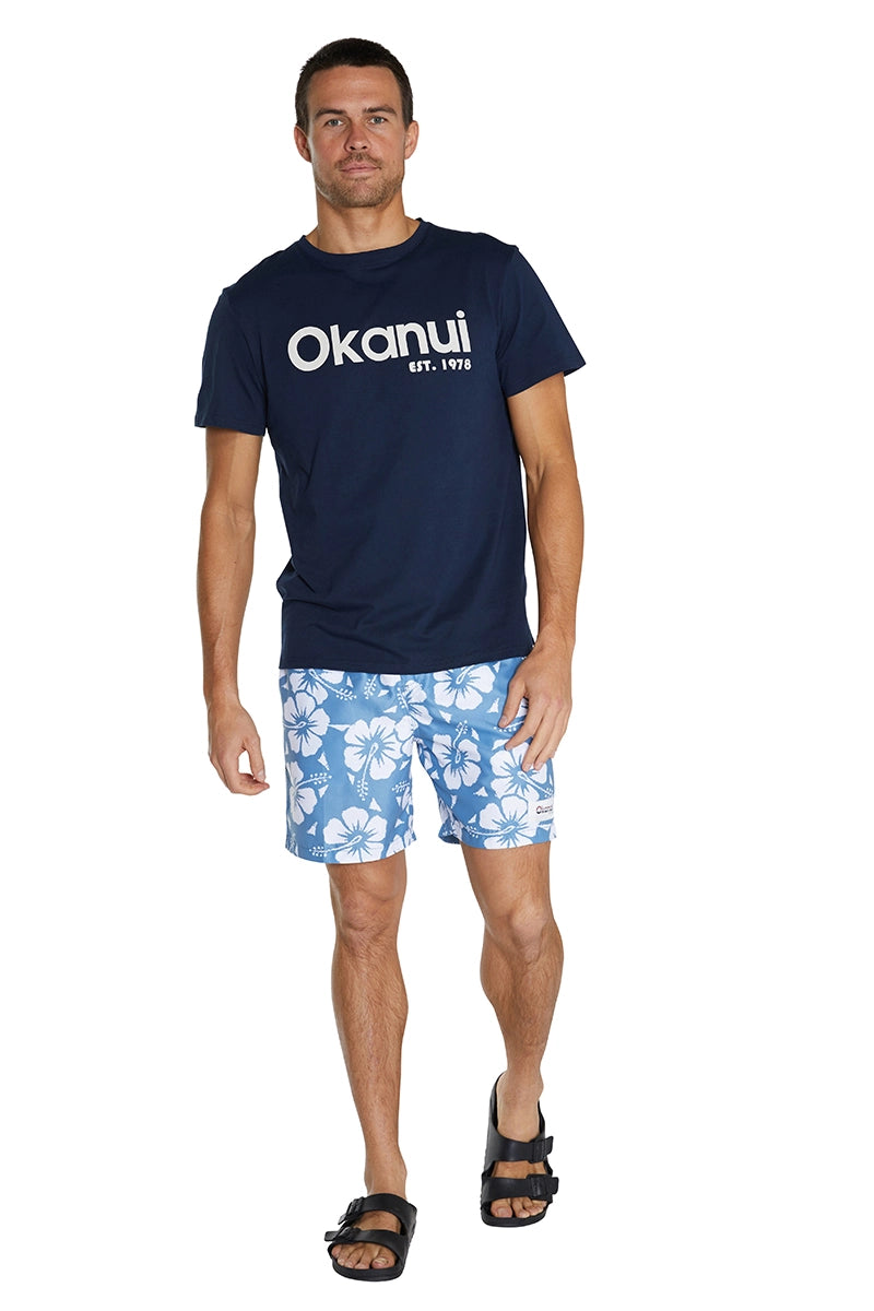 A male model posing and wearing the Okanui Classic Swim Shorts and the Okanui Logo Tee.