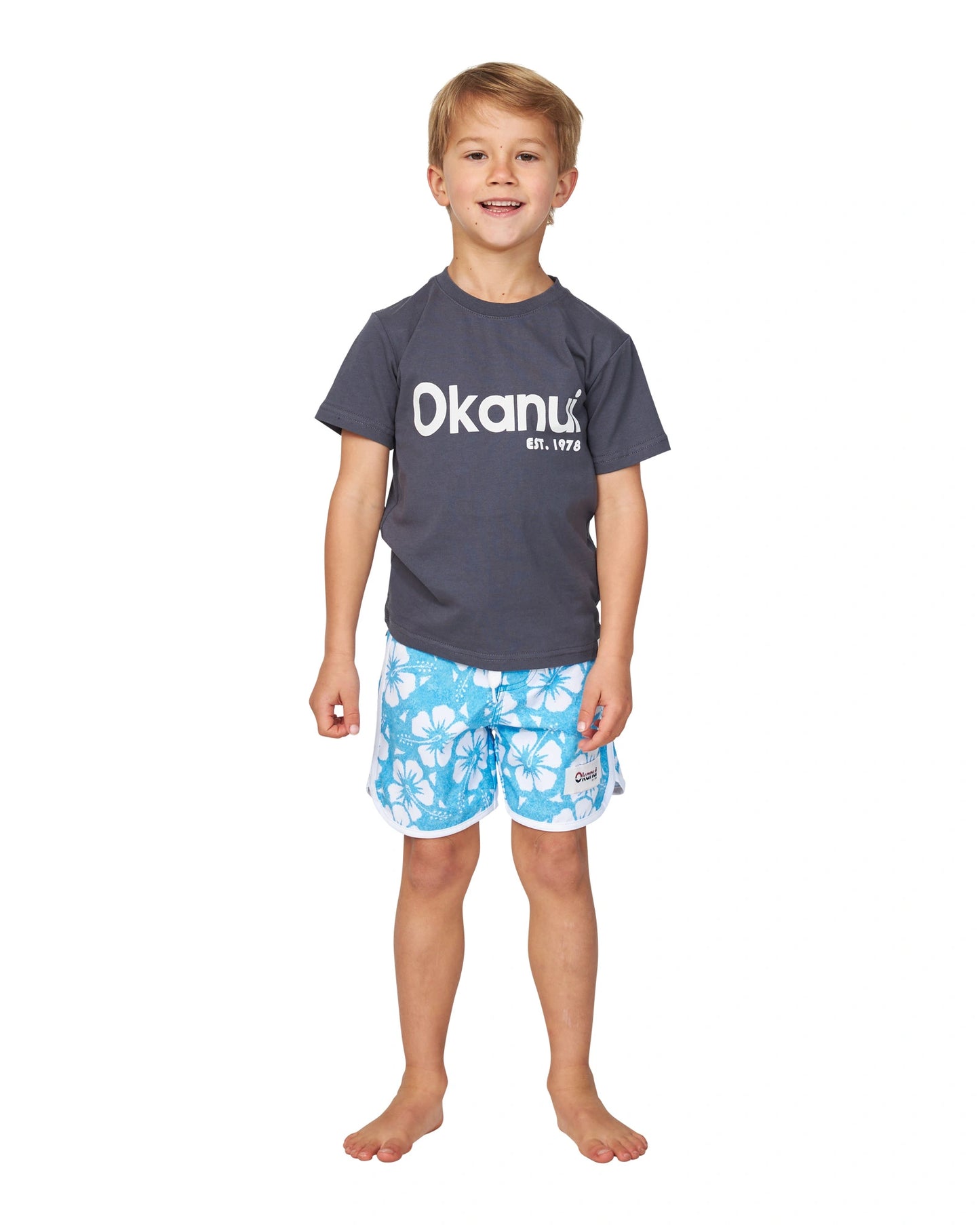 Full body front view of a little boy wearing the Okanui Logo Tee T-shirt in Washed Black