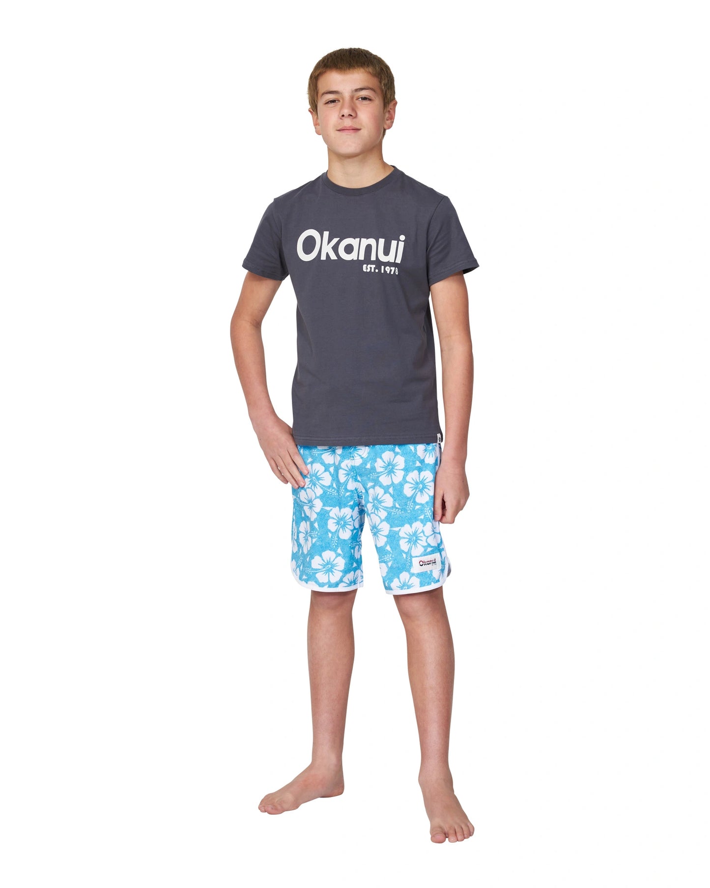 Full body front view of a boy wearing the Okanui Logo Tee T-shirt in Washed Black