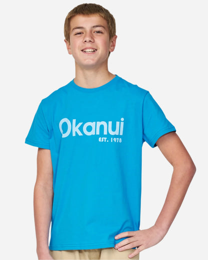 Full body close up view of a boy wearing the Okanui Logo tee T-shirt in Washed Blue