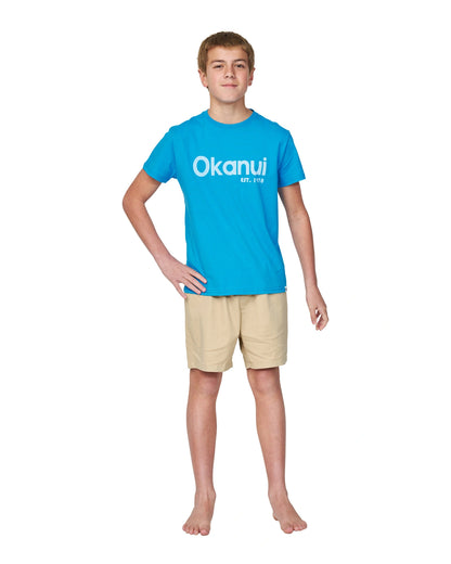 Full body front view of a boy with his hand on the hip pose wearing the Okanui Logo tee T-shirt in Washed Blue