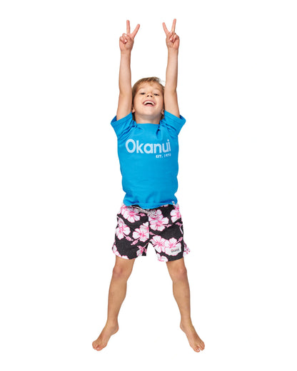 Full body front view of a boy hands up peace sign pose wearing the Okanui Logo tee T-shirt in Washed Blue