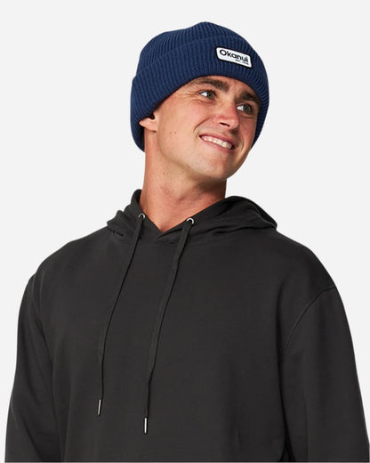 Front view of a male model in a hooded shirt wearing the Okanui Fishermans rib knit beanie hat in navy color