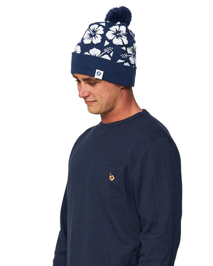 Left Side view of a male model in long sleeves wearing the Okanui Hibiscus Rib knit Pom Pom beanie hat in Navy color