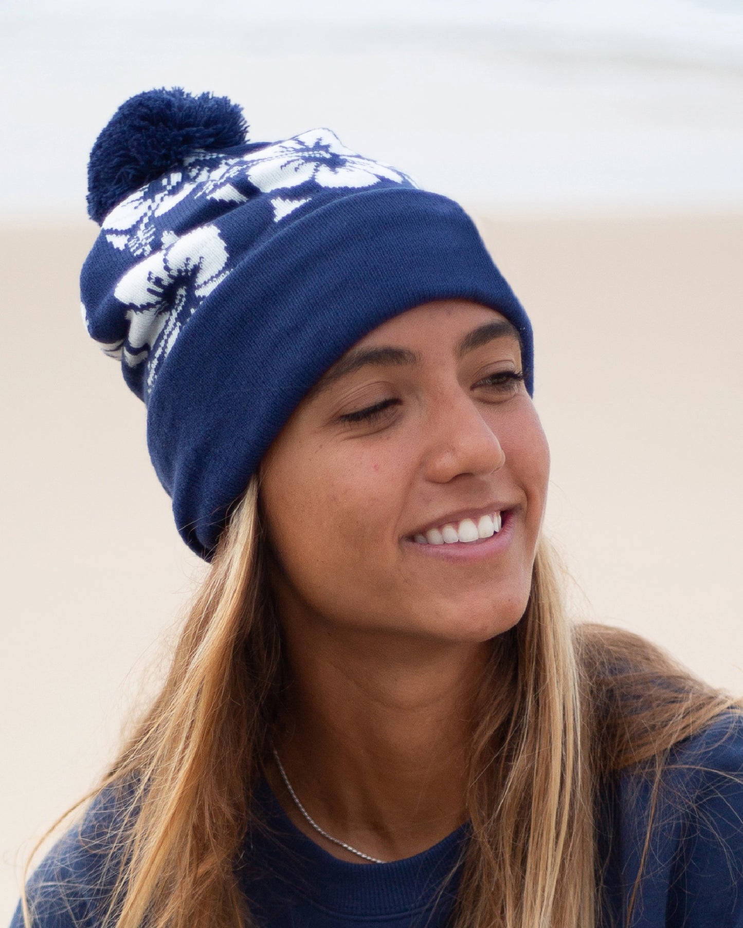 Close up view of a female model wearing the Okanui Hibiscus Rib knit Pom Pom beanie hat in Navy color