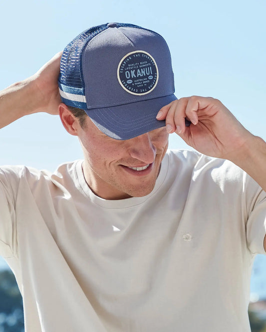 A male model wearing the Okanui Post trucker cap in Iron