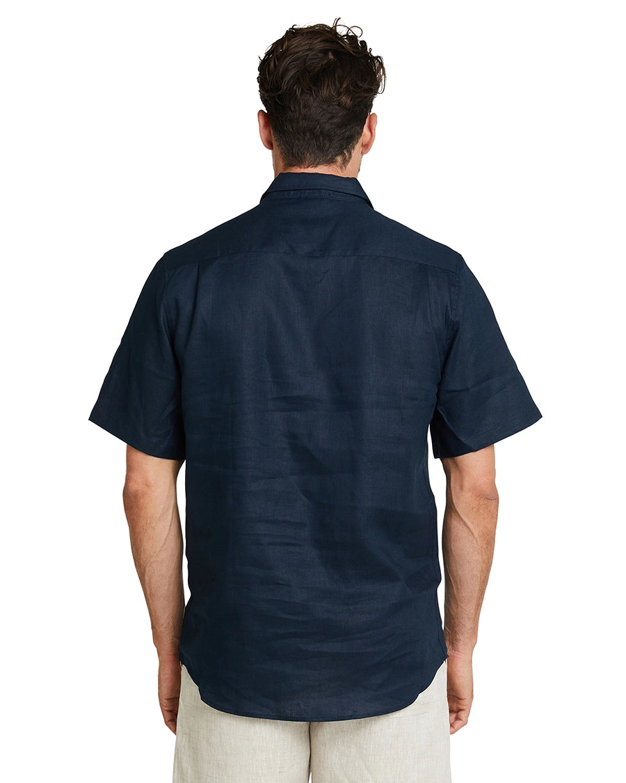 A back view of a male model posing and wearing the Okanui Linen Short Sleeve shirt in navy.