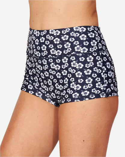 A woman wearing a surf short in hibiscus navy blue showing the side details. 