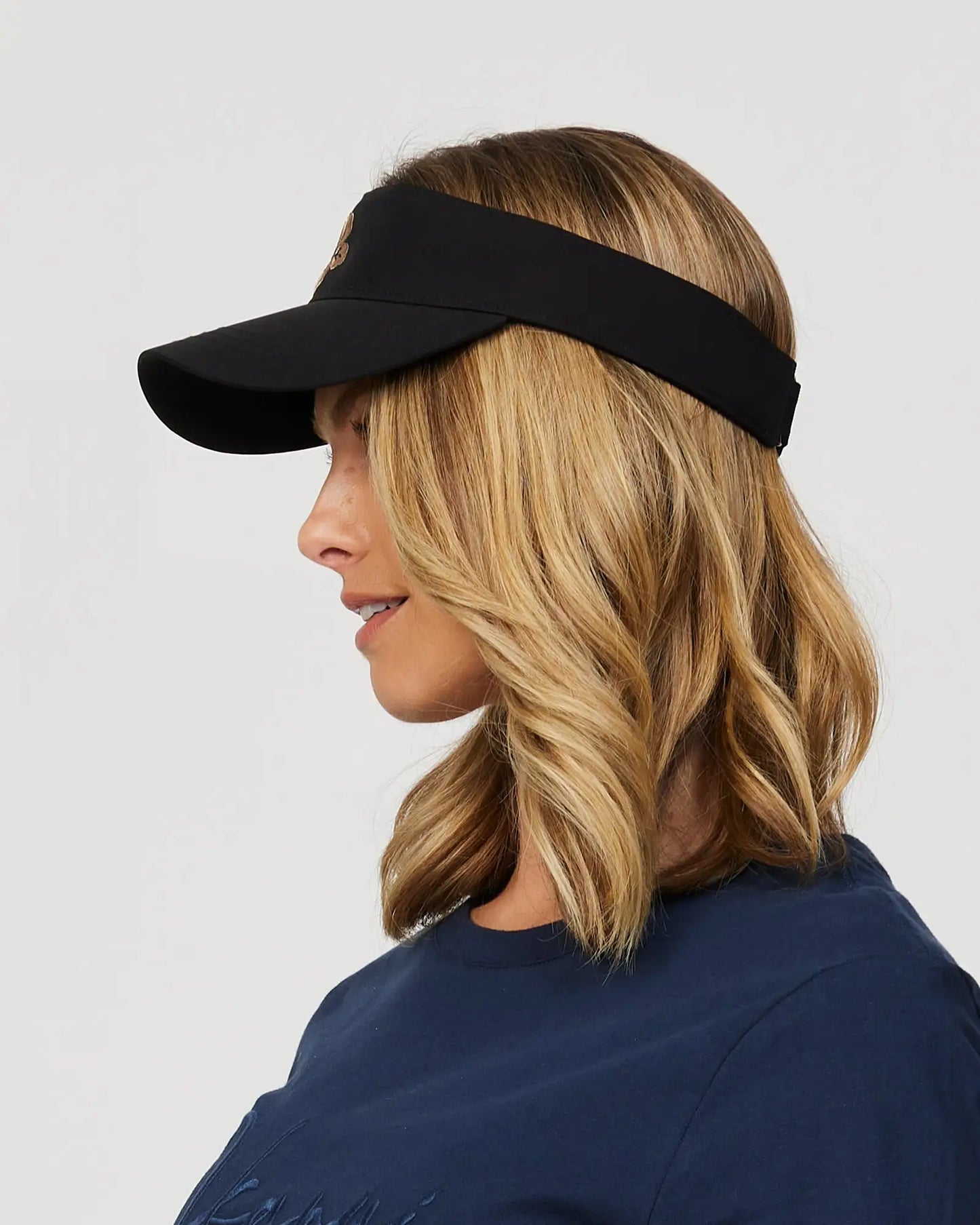 Left side view of a female model wearing the Okanui Ikon Visor Cap in Black